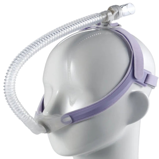 A nasal pillow mask system, designed for women, mounted on a mannequin head. The mask has a clear frame with purple and gray straps, and it includes a flexible tube for air delivery.